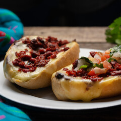 Mexican molletes with chorizo and fresh sauce on wooden background
