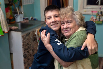 Happy, smiling grandson hugs his grandmother in the kitchen at home. Happy family relationships,...