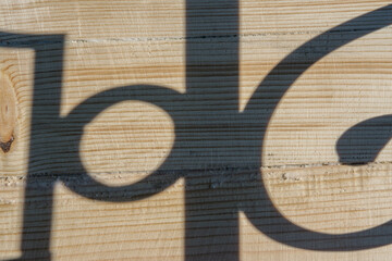 A wooden background against which a curly shadow falls with straight and rounded lines in sunny weather.