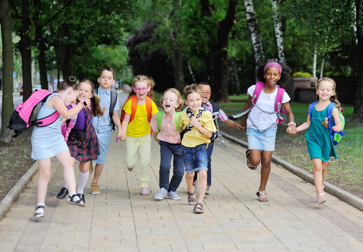 a group of school children of different races in colorful clothes with school bags and backpacks run to school against the background of green m Park. Back to school, knowledge day, 