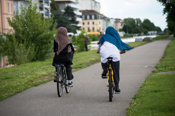 Portrait on back view of veiled women on bicycle on bike lane in border water