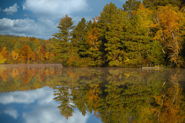autumn day clouds and fall colored trees reflection in calm lake water. 