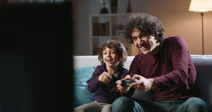 Cute authentic asian brothers with curled hair enjoying their together time, playing football video games in front of tv, parent and son relaxing with their hobby 4k footage