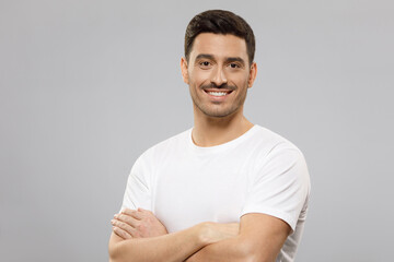Young handsome smiling man wearing white blank t-shirt, standing with crossed arms, isolated on...