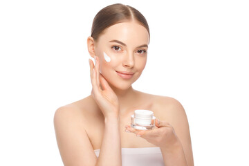Young beautiful woman with clear skin holding cosmetic jar and applying face cream, isolated on white background. Concept of female beauty