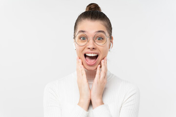 Fototapeta premium Young woman screaming with joy, feeling shocked by commercial offer, touching cheeks with palms, looking at camera with open mouth, isolated on gray background