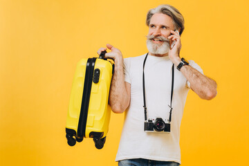 Stylish bearded man with camera laughing while holding a yellow suitcase chatting on the phone