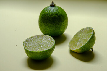 close up on green lemon fruit and halves over a yellow background
