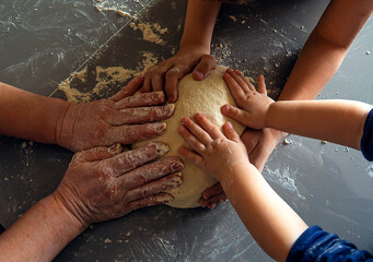 The big hands of an old woman, the middle hands of a boy and the small hands of a girl hold bread dough. The intergenerational connection. Different ages together. Digital detox and mental health.