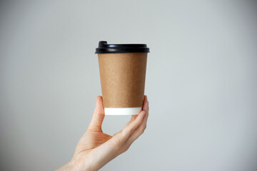 Disposable cardboard cup with empty space for text in human hand on gray background. Take out coffee or delivery service. Copy space.