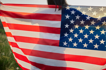 4th of July. Fourth of July. American woman with the national American flag against beautiful landmark. Independence Day. Patriotic holiday, democracy respect and veteran respect concept