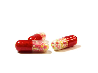 Close-up of half transparent red capsules with dragees inside isolated on a white background.