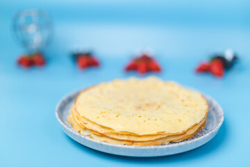 Close-up of a pack of French Crepes in a serving plate with berries on the side on a blue background. Crepe with strawberries, blueberries, rose berries, sliced bananas.