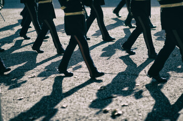 Troop of royal guards marching in close-up on textured pavement with dramatic shadows in London, England, UK