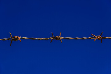 Imprisoned concept. Barbed wire strands with rust and blue sky as background