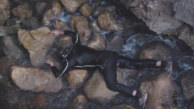 Aerial top view of the almost drowned man lying on the stony sea shore and breathing. Stock. Barely alive man lying on his stomach on big stones, SOS concept.