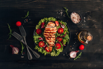 Fototapeta na wymiar Grilled chicken fillet and fresh vegetable salad of tomatoes and arugula leaves. Healthy food. Black background.