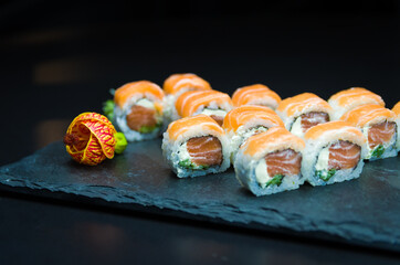 Sushi, traditional Japanese cuisine. Delicious Uramaki on decorated plate, black background.