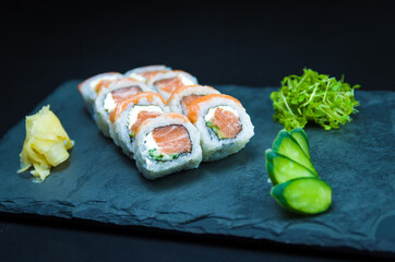 Sushi, traditional Japanese cuisine. Delicious Uramaki on decorated plate, black background.