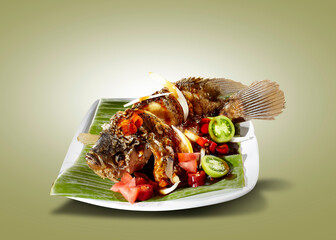 Ketchup fried fish is served on a white plate with a banana leaf.