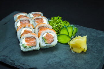 Sushi, traditional Japanese cuisine. Delicious Uramaki on decorated plate, black background.