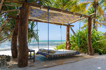 Wooden swing with a mattress and pillows under a canopy on the tropical beach near sea, island...