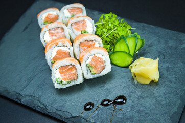 Sushi, traditional Japanese cuisine. Delicious Uramaki on decorated plate, black background.