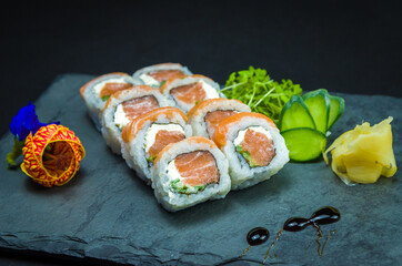 Sushi, traditional Japanese cuisine. Delicious Uramaki on decorated plate, black background.