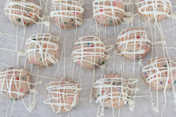 Birthday cake sprinkled edible cookie dough balls with vanilla drizzle on white parchment paper.