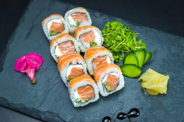 Sushi, traditional Japanese cuisine. Delicious Uramaki on decorated plate, black background.