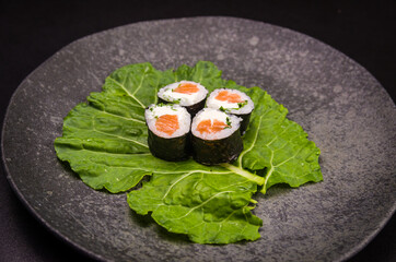 Sushi, traditional Japanese cuisine. Delicious hossomaki on the decorated plate, black background.