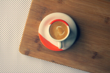 Freshly brewed sparkling coffee in a small orange and white mug. Cup with typical Brazilian drink on a wooden board. Copy space.