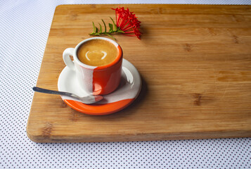 Freshly brewed sparkling coffee in a small orange and white mug. Cup with typical Brazilian drink on a wooden board. Copy space.