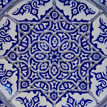 Traditional Moroccan hand painted embellished plate decorated with ornate silver filigree at a pottery shop in Fes, Morocco