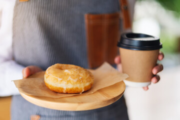 A waitress holding and serving a piece of homemade donut in wooden tray and a paper cup of coffee