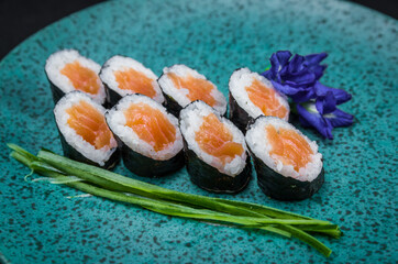 Sushi, traditional Japanese cuisine. Delicious hossomaki on the decorated plate, black background.