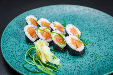 Sushi, traditional Japanese cuisine. Delicious hossomaki on the decorated plate, black background.
