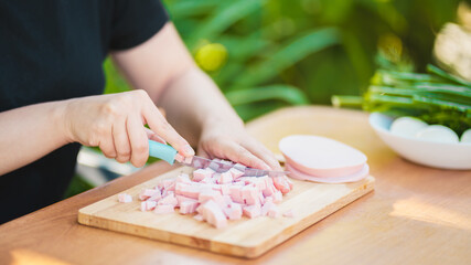Young woman cutting sausage on wooden board outdoors. Women's hands cutting sausage goods with knife on chopping board.