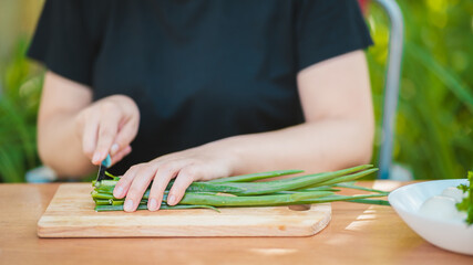 Fototapeta na wymiar Close-up of woman cutting green onion on wooden board outdoors. Women's hands cutting verdure with knife on chopping board.