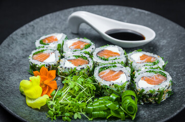 Perfect sushi, traditional Japanese cuisine. Delicious uramaki with shoyo sauce on the decorated plate, black background.