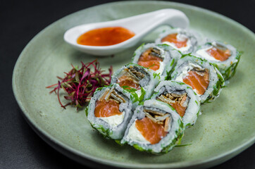 Perfect sushi, traditional Japanese cuisine. Delicious uramaki with sweet and sour sauce on the decorated plate, black background.