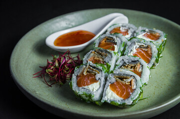 Perfect sushi, traditional Japanese cuisine. Delicious uramaki with sweet and sour sauce on the decorated plate, black background.
