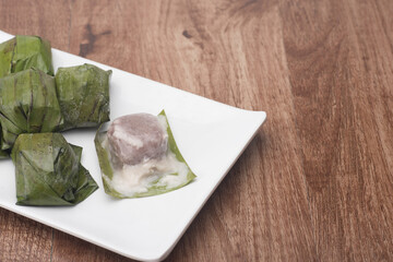 Koci the malaysian glutinous rice ball served in banana leaf on white plate over wooden table