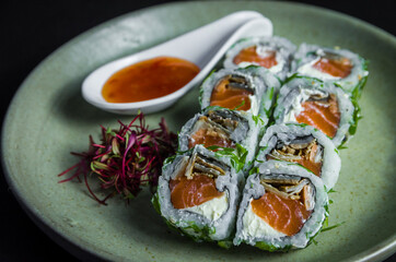 Perfect sushi, traditional Japanese cuisine. Delicious uramaki with sweet and sour sauce on the decorated plate, black background.