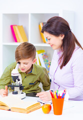 The boy and his mother are working with a microscope. The student looks through the eyepiece of the...