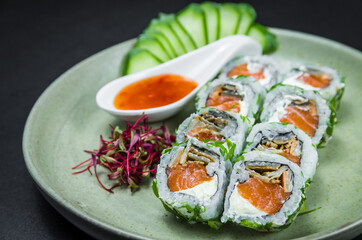 Perfect sushi, traditional Japanese cuisine. Delicious uramaki with sweet and sour sauce on the decorated plate, black background.
