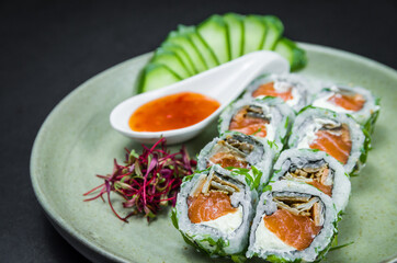 Perfect sushi, traditional Japanese cuisine. Delicious uramaki with sweet and sour sauce on the decorated plate, black background.