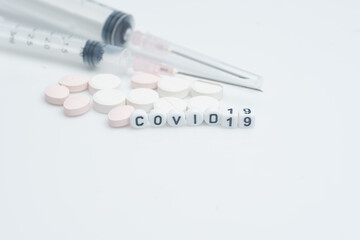 The word covid 19 with pills and syringes,over white background and surface