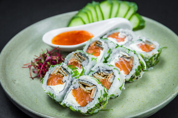 Perfect sushi, traditional Japanese cuisine. Delicious uramaki with sweet and sour sauce on the decorated plate, black background.