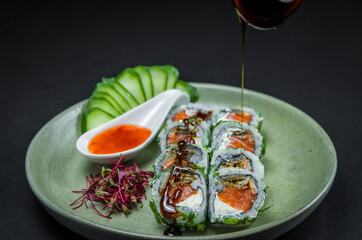 Perfect sushi, traditional Japanese cuisine. Delicious uramaki with sweet and sour sauce on the decorated plate, black background.